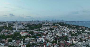 Establishing orbiting aerial drone shot of a Hagia Sophia Holy Grand Mosque with Bosphorus bridge and city skyline with a flag on the background in Fatih, Istanbul, Turkey at sunset. photo