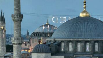 Establishing orbiting aerial drone shot of a Hagia Sophia Holy Grand Mosque with Bosphorus bridge and city skyline with a flag on the background in Fatih, Istanbul, Turkey at sunset. photo