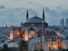 Establishing orbiting aerial drone shot of a Hagia Sophia Holy Grand Mosque with Bosphorus bridge and city skyline with a flag on the background in Fatih, Istanbul, Turkey at sunset. photo