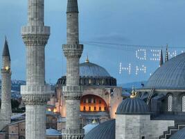 Establishing orbiting aerial drone shot of a Hagia Sophia Holy Grand Mosque with Bosphorus bridge and city skyline with a flag on the background in Fatih, Istanbul, Turkey at sunset. photo