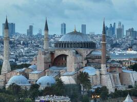 Establishing orbiting aerial drone shot of a Hagia Sophia Holy Grand Mosque with Bosphorus bridge and city skyline with a flag on the background in Fatih, Istanbul, Turkey at sunset. photo