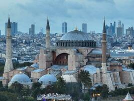 Establishing orbiting aerial drone shot of a Hagia Sophia Holy Grand Mosque with Bosphorus bridge and city skyline with a flag on the background in Fatih, Istanbul, Turkey at sunset. photo