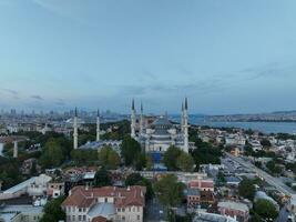 Establishing orbiting aerial drone shot of a Hagia Sophia Holy Grand Mosque with Bosphorus bridge and city skyline with a flag on the background in Fatih, Istanbul, Turkey at sunset. photo