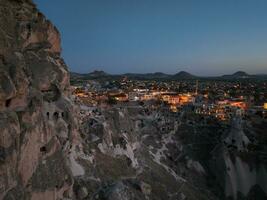 Aerial view of natural rock formations in the sunset, valley with cave houses in Cappadocia, Turkey. Natural landscape city lights at the night. photo