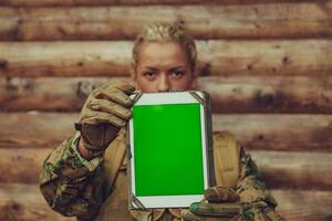 Woman soldier using tablet computer against old wooden wall in camp photo