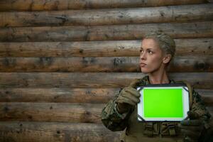 Woman soldier using tablet computer against old wooden wall in camp photo