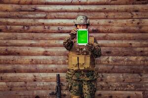 Woman soldier using tablet computer against old wooden wall in camp photo