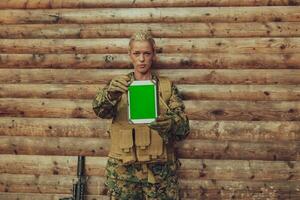 Woman soldier using tablet computer against old wooden wall in camp photo