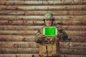 Woman soldier using tablet computer against old wooden wall in camp photo