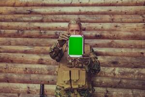 mujer soldado utilizando tableta computadora en contra antiguo de madera pared en acampar foto