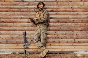 soldado utilizando tableta computadora en contra antiguo de madera pared en militar acampar a permanecer en contacto con amigos y familia foto