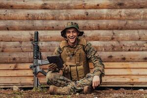 Soldier using tablet computer against old wooden wall in military camp to stay in contact with friends and family photo