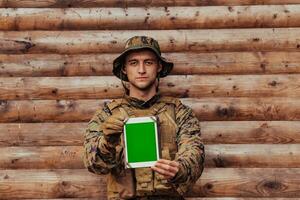 Soldier using tablet computer against old wooden wall in military camp to stay in contact with friends and family photo