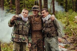 equipo de soldados y terrorista tomando selfie con teléfono inteligente en el bosque foto