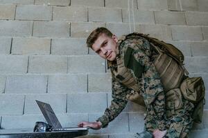 American soldier in military uniform using laptop computer for drone controlling and to stay in contact with friends and family photo