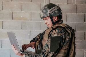 American soldier in military uniform using laptop computer for drone controlling and to stay in contact with friends and family photo