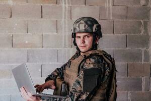 American soldier in military uniform using laptop computer for drone controlling and to stay in contact with friends and family photo