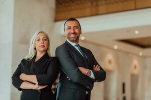 Portrait photo of businessman and businesswoman with crossed arms standing in modern corporation. Selective focus