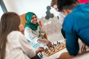 Multiethnic group of business people playing chess while having a break in relaxation area at modern startup office. Selective focus photo