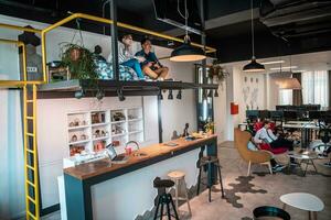 Group of casual multiethnic business people taking break from the work doing different things while enjoying free time in relaxation area at modern open plan startup office photo