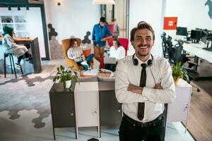 Portrait of successful businessman entrepreneur with headphones around his neck and colleagues in the background at busy startup office photo