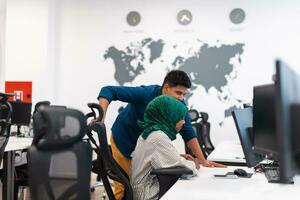 Multiethnic startup business team Arabian woman wearing a hijab on meeting in modern open plan office interior brainstorming, working on laptop and desktop computer. Selective focus photo