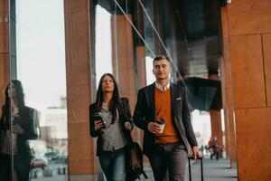 Business man and business woman talking and holding luggage traveling on a business trip, carrying fresh coffee in their hands.Business concept photo