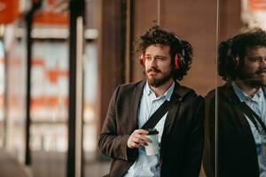 Trendy businessman with leather briefcase in financial district using smartphone while listening audio songs headphones drinking coffee photo