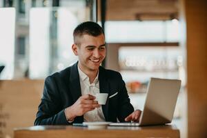 Happy business man sitting at cafeteria with laptop and smartphone photo