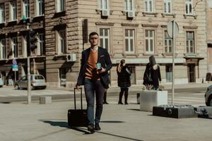 ir a la terminal del aeropuerto. viajero de negocios confiado caminando por las calles de la ciudad y tirando de su maleta bebiendo café y hablando en el teléfono inteligente foto