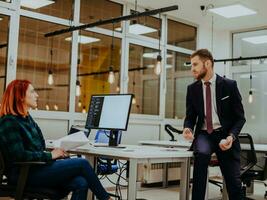 The boss of the company is talking to his colleague who is working on a project in a modern office photo