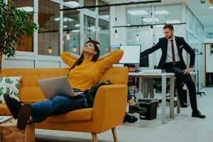 Handsome businesswoman employee sitting on a yellow couch while working on her laptop in startup company. photo