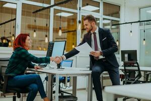 The boss of the company is talking to his colleague who is working on a project in a modern office photo
