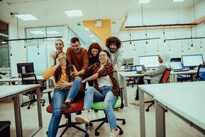 Team building and office fun. Young cheerful businesspeople in smart casual wear having fun while racing on office chairs and smiling. photo