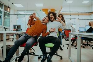 Team building and office fun. Young cheerful businesspeople in smart casual wear having fun while racing on office chairs and smiling. photo