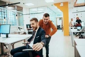 Team building and office fun. Young cheerful businesspeople in smart casual wear having fun while racing on office chairs and smiling. photo