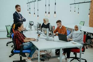 Group of multi-ethnic colleagues working on desktop computers, laptop and sharing their ideas in a modern office space.Young influencers work on online marketing projects. photo