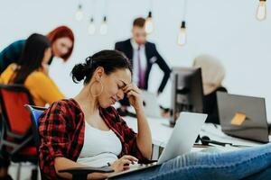 cansado mujer de negocios sentado en un oficina y trabajando en su ordenador portátil foto