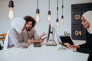 Group of multi-ethnic colleagues working on desktop computers, laptop and sharing their ideas in a modern office space.Young influencers work on online marketing projects. photo