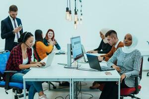 grupo de multiétnico colegas trabajando en escritorio ordenadores, ordenador portátil y compartiendo su ideas en un moderno oficina espacio.joven influencers trabajo en en línea márketing proyectos foto