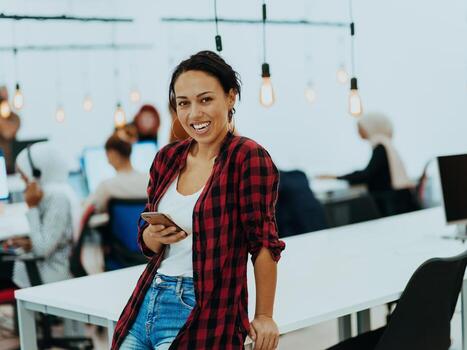 Woman sitting at workplace desk holds smartphone staring at laptop, synchronize data between computer and gadget in office, using corporate devices and business application, plan work, using organizer photo