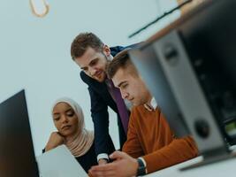 Group of multi-ethnic colleagues working on desktop computers, laptop and sharing their ideas in a modern office space.Young influencers work on online marketing projects. photo