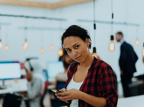 Woman sitting at workplace desk holds smartphone staring at laptop, synchronize data between computer and gadget in office, using corporate devices and business application, plan work, using organizer photo