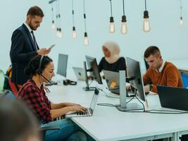 Group of multi-ethnic colleagues working on desktop computers, laptop and sharing their ideas in a modern office space.Young influencers work on online marketing projects. photo