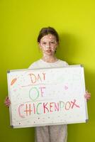 A little schoolgirl with chickenpox draws a message on the whiteboard in the kids' room, and antiseptic cream is applied to the face and body. Chalkboard background. photo