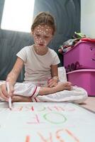 Little school girl with chickenpox drawing on white board in kids' room, antiseptic cream applied to face and body. Chalkboard and toys background. photo