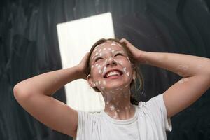 Portrait of a little school girl with chickenpox, antiseptic cream applied to face and body .Chalkboard background. photo