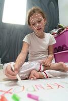 Little school girl with chickenpox drawing on white board in kids' room, antiseptic cream applied to face and body. Chalkboard and toys background. photo