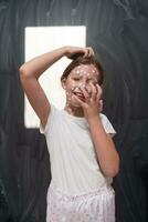 Portrait of a little school girl with chickenpox, antiseptic cream applied to face and body .Chalkboard background. photo