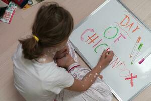 Top view of Little school girl with chickenpox drawing on white board in kids' room, antiseptic cream applied to face and body. Chalkboard and toys background. photo